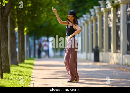 Sur le rythme. Danseuse de rue dans un parc urbain frappant la posture confiante sous l'ombre des arbres Banque D'Images
