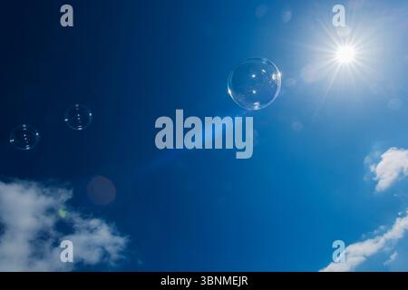 Bulles de savon dans le ciel bleu avec des nuages individuels rétroéclairés par le soleil. Banque D'Images