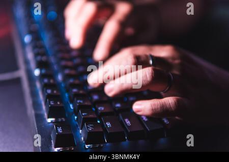Gros plan mains tapant sur un clavier mécanique avec rétroéclairage LED dans une pièce sombre. Banque D'Images