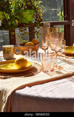 Une table d'été lumineuse décorée de citrons, d'hortensias vertes et de verrerie. La lumière du soleil déverse à travers les plantes suspendues, créant une atmosphère chaleureuse et joyeuse Banque D'Images