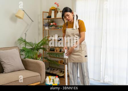Femme au foyer asiatique activement engagée dans les tâches ménagères quotidiennes, telles que le nettoyage, l'organisation ou le rangement de sa maison. Banque D'Images