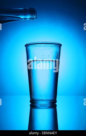 Bouteille au-dessus du verre d'eau douce sur fond bleu dégradé. Rétroéclairé Banque D'Images