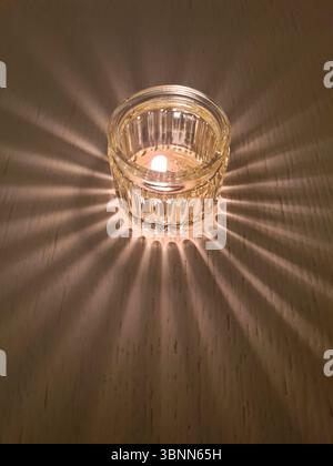 Une bougie dans le verre forme une ombre sur une table en bois dans la demi-obscurité Banque D'Images