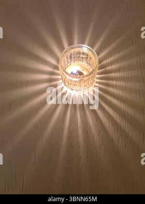 Une bougie dans le verre forme une ombre sur une table en bois dans la demi-obscurité Banque D'Images
