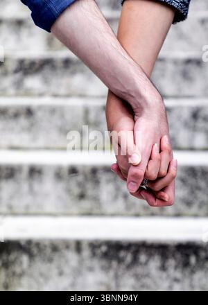 Un couple tient les mains, les doigts entrelacés, avec un anneau visible sur une des mains. Banque D'Images