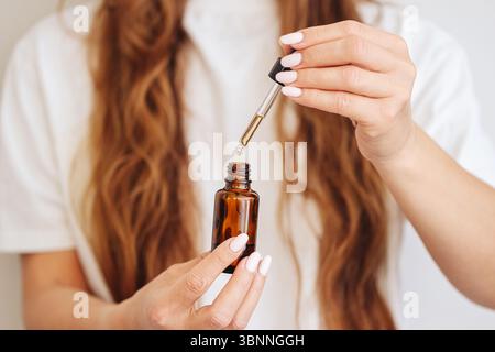 Femme utilisant un flacon compte-gouttes. Gros plan des mains avec une pipette. Soin naturel ou huile essentielle. Routine beauté avec sérum. Traitement cosmétique. Banque D'Images