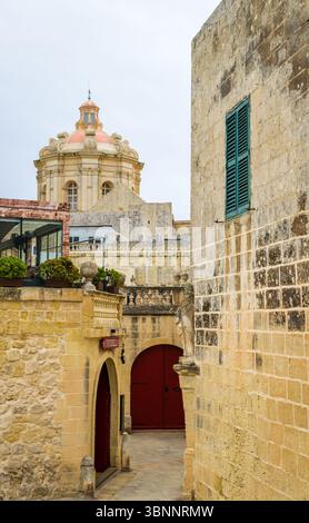 Rabat, Malte - 10 février 2024 : vue panoramique de la coupole de la cathédrale de Paul à Mdina à travers les toits de la ville silencieuse, avec rue en premier plan Banque D'Images