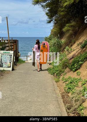 Groupe de surfeurs portant des planches le long d'un chemin vers la plage sur l'île de São Miguel, Açores, Portugal. La route pittoresque est bordée par une falaise luxuriante. Banque D'Images