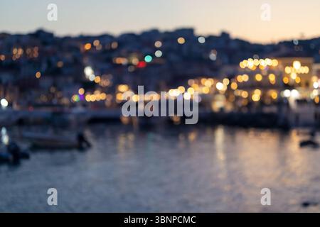 bokeh doux des bâtiments illuminés et des reflets sur l'eau dans une scène côtière floue en soirée, parfait pour les thèmes d'arrière-plan ou abstraits. Banque D'Images