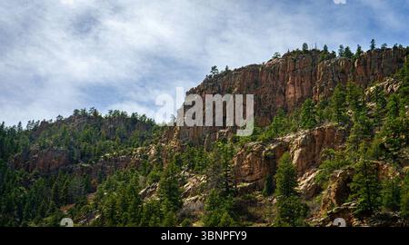 Des falaises rouges déchiquetées s'élèvent au-dessus d'une dense forêt de pins le long de Phantom Canyon Road près de Cañon City, Colorado. La géologie dramatique met en valeur le chemin moins connu. Banque D'Images