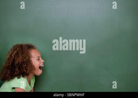 La fille se penche en avant avec les cheveux bouclés contre le tableau vert dans la conception plate, montrant la bouche ouverte Banque D'Images