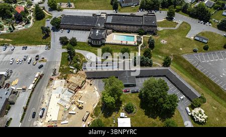 Vue aérienne d'Un chantier de construction occupé avec charpente en bois et matériaux de construction sur Une journée ensoleillée, entouré de champs verts, bâtiments résidentiels Banque D'Images