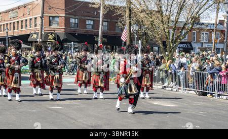 Lindenhurst, New York, États-Unis, le 30 mars 2024 - Un groupe de cornemuse habillés de kilts écossais traditionnels et de chapeaux en peau de Bearskin se produit dans Une rue colorée Banque D'Images