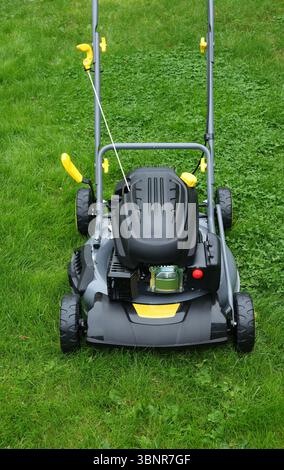 Nouvelle tondeuse à gazon dans le jardin longue herbe verte, prête pour le travail de coupe, verticale Banque D'Images