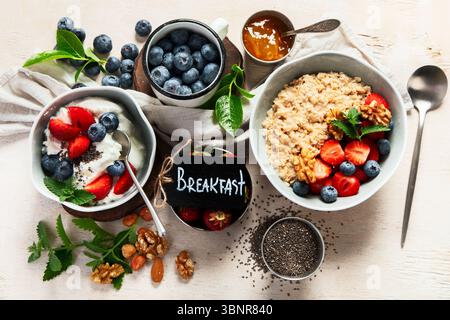 Ingrédients biologiques pour un petit déjeuner sain - yaourt, noix, fruits frais, flocons d'avoine, flocons de grains entiers sur fond blanc. Vue de dessus. Banque D'Images