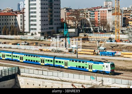 Milan, Italie - 19 mars 2025 : le train Trenord passe devant le chantier de construction du village olympique près de la Fondazione Prada Banque D'Images