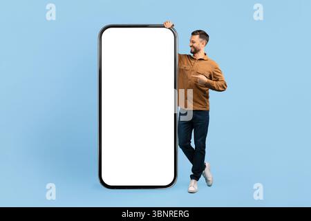 Jeune homme souriant pointant vers un énorme écran blanc de maquette de smartphone géant Banque D'Images