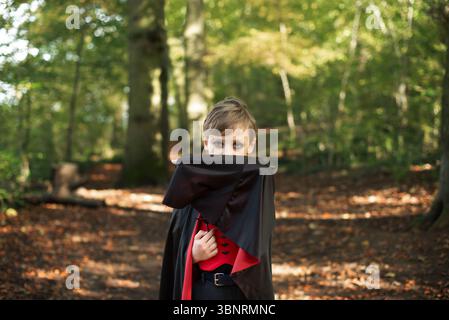 Garçon vampire cachant son visage avec manteau dans la forêt effrayante. Banque D'Images