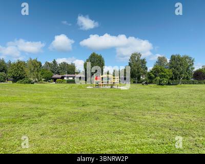 Une scène de parc sereine avec une aire de jeux, des arbres et une maison sous un ciel bleu vif, Östersund Suède Banque D'Images