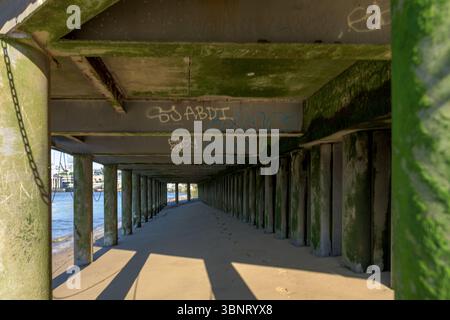 Royaume-Uni, Londres, 09 juillet 2025. Vue sous une passerelle le long de la Tamise à marée basse, avec des piliers couverts de mousse et des ombres projetées sur l'australie méridionale Banque D'Images