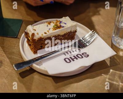 Royaume-Uni, Londres, 09 juillet 2025. Une tranche de gâteau aux carottes servi dans une assiette chez SOHO Coffee Co., avec une fourchette reposant sur une serviette de marque dans un CA confortable Banque D'Images