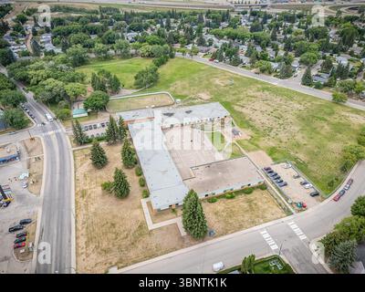 Grand terrain vide avec un bâtiment scolaire au milieu. Le lot est entouré d'une clôture et dispose d'un parking avec plusieurs voitures Banque D'Images