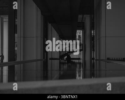Londres, Royaume-Uni, 11 décembre 2024. Couloir faiblement éclairé dans un bâtiment d'entreprise dans le quartier financier, avec de fortes ombres et une symétrie géométrique Banque D'Images