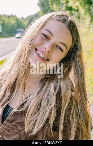 Une jeune femme aux longs cheveux blonds sourit brillamment pour la caméra Banque D'Images