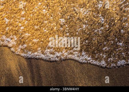 L'eau cristalline lavant doucement le sable doré sur la rive du lac Tahoe, créant de beaux motifs Banque D'Images