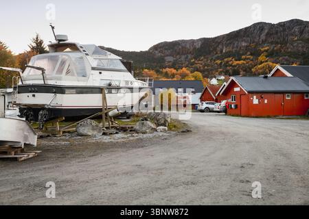 Un bateau blanc repose sur le rivage dans un village confortable entouré de montagnes et de teintes automnales. Vue sur la rue du village de pêcheurs norvégien Banque D'Images