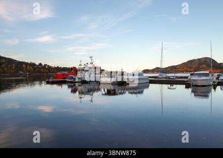 Reflet de bateaux amarrés dans des eaux tranquilles dans une marina norvégienne pittoresque avec une toile de fond de montagne, capturé au coucher du soleil dans un climat serein d'automne Banque D'Images
