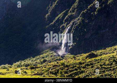 Cascade dans la vallée d'Engelberg, canton d'Uri. Une cascade impressionnante descend en cascade une paroi rocheuse sombre près de Niedersurenen dans le canton d'Uri, en Suisse, près d'Engelberg. Le soleil illumine l'eau en cascade et la pulvérisation qui en résulte, tandis que le premier plan se compose d'une pente verte ensoleillée avec des rochers Banque D'Images