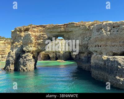 L’arche rocheuse de l’Arco de Albandeira et les grottes marines sont montrées le long de la région sud de l’Algarve, au Portugal, près de la ville de Porches, pendant une journée ensoleillée. Banque D'Images