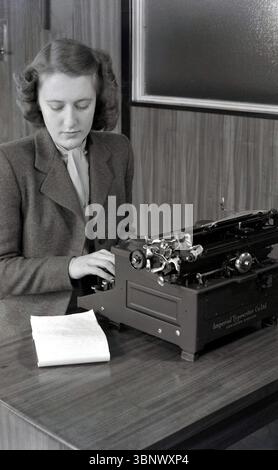 Années 1940, jeune femme historique, élégante, costume en laine et foulard, une secrétaire utilisant une machine à écrire, faite par l'Imperial Typewriter Co de Leicester, Angleterre, Royaume-Uni, tapant une lettre d'un cahier avec un raccourci sur le bureau. Banque D'Images