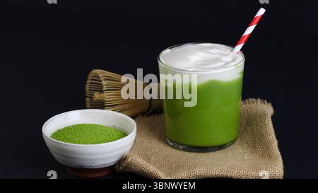 Latte Matcha glacé avec mousse crémeuse et paille rouge sur fond foncé - esthétique du thé japonais Banque D'Images