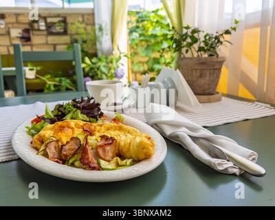 Scène de petit déjeuner appétissante avec omelette moelleuse bacon croustillant et salade du jardin dans le café ensoleillé Banque D'Images
