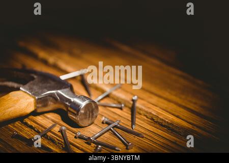 Marteau avec poignée en bois est couché à plat sur l'établi en rendu 3D, avec des clous en acier dispersés Banque D'Images