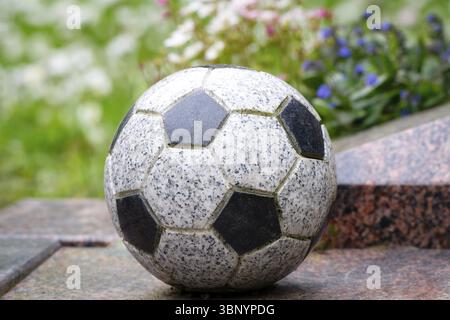 Un ballon de football en pierre comme décoration sur une tombe devant des fleurs colorées dans un fond flou Banque D'Images