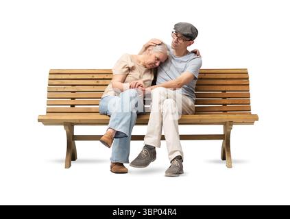 Couple mûr assis sur un banc en bois, l'homme réconfortant son partenaire qui semble triste ou en détresse. Il l'embrasse avec soin, offrant des s émotionnels Banque D'Images