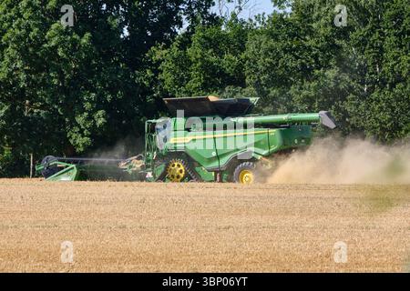 4 juillet 2025 - Lauterbach-Allemagne : une moissonneuse-batteuse John Deere travaille à travers un champ d'orge, soulevant la poussière pendant qu'elle récolte sous un ciel dégagé avec du tré Banque D'Images