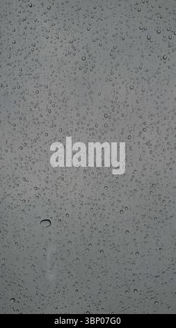 Une vue tranquille à travers une fenêtre imbibée de pluie affichant de jolies gouttelettes d'eau minuscules sur verre sous un ciel sombre parfait pour réfléchir sur la nature Banque D'Images