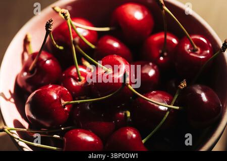 Cerises rouges fraîches dans un bol en céramique. Fruits mûrs juteux avec des tiges. Collation estivale saine pleine de vitamines et d'antioxydants. Nourriture naturelle délicieuse. Banque D'Images