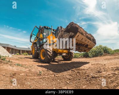 Le chargeur de tracteur jaune transporte du sol depuis le chantier de construction. Zone de dégagement pour la construction Banque D'Images