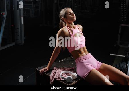 Forme jeune femme relaxant après une séance d'entraînement intense à la salle de gym montrant la définition musculaire de récupération et un mode de vie actif sain Banque D'Images