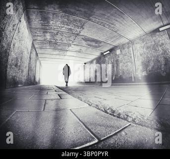 Homme légèrement plié en silhouette marchant dans un tunnel de béton urbain. Banque D'Images