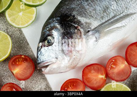Poisson Dorado entier frais avec citrons verts coupés et tomates. Banque D'Images
