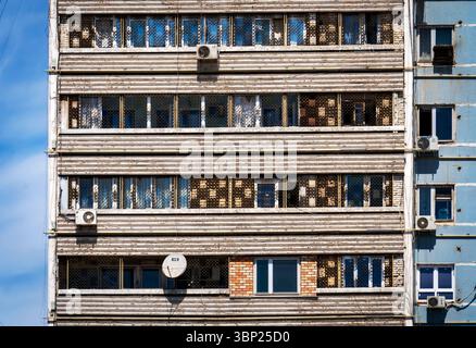 Vue rapprochée de la façade d'un immeuble d'habitation altérée, dotée de plusieurs fenêtres, de climatiseurs et d'une antenne parabolique. Le bâtiment montre Banque D'Images