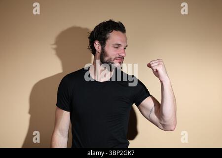 Un homme barbu dans un t-shirt noir regarde attentivement son poing serré, tenu à sa gauche, suggérant un moment de contemplation sur la force, Banque D'Images