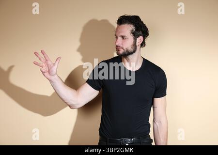 Un jeune homme portant un t-shirt noir affiche quatre doigts sur sa main tout en regardant vers sa main ou de côté, indiquant le chiffre quatre ou comptant. Goujon Banque D'Images