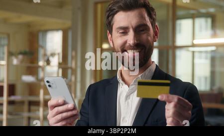 Business souriant homme caucasien payant la carte de crédit à l'aide d'un téléphone mobile dans le bureau homme gestionnaire entrepreneur acheteur application bancaire Guy pdg leader cashless Banque D'Images